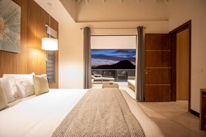 Ein Hotelzimmer mit großem Bett, Blick auf die Stadt bei Einbruch der Dunkelheit, einem Balkon mit Sitzgelegenheit und einem Holzschrank.