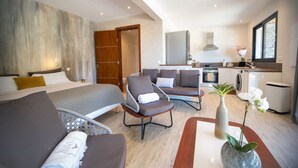A modern hotel room with a bed, seating area, kitchenette, and a large window.