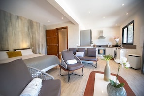 Ein modernes Hotelzimmer mit Bett, Sitzecke, Küchenzeile und großem Fenster.