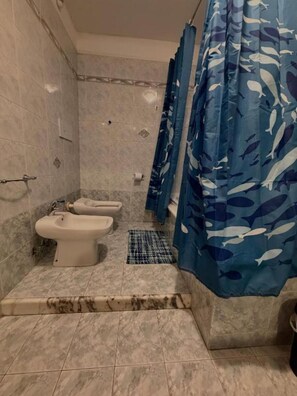 Une salle de bain avec deux bidet, un rideau de douche ornĂ© dâun motif de poissons et un sol carrelĂ©.