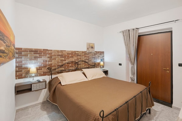 A bedroom with a brick-patterned headboard, a bed with a brown bedspread, a nightstand with a lamp, and a wooden door.