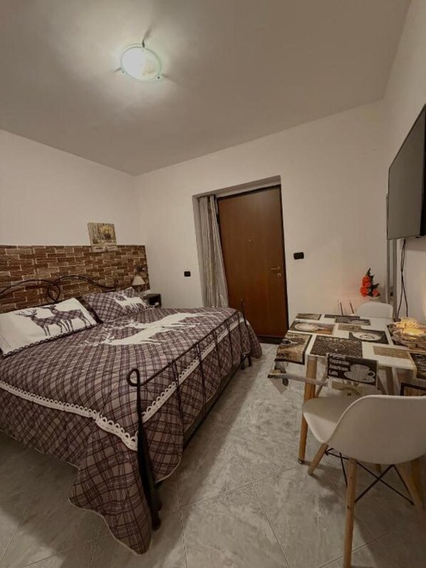 Ein Schlafzimmer mit einem Bett, einem Tisch mit Stühlen, einem Fernseher und einer Tür.