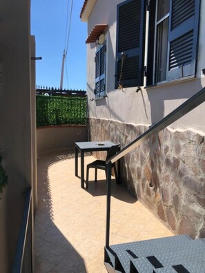 Un petit patio extĂ©rieur, avec un mur en pierre, un escalier en mĂ©tal et une petite table accompagnĂ©e dâune chaise.