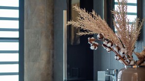 Ein modernes Interieur mit einer Tischvase mit getrockneten Pflanzen, einem Fenster mit Jalousien und einer Küchenzeile im Hintergrund.