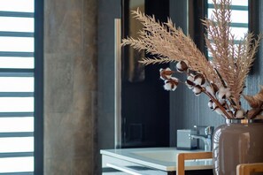 Ein modernes Interieur mit einer Tischvase mit getrockneten Pflanzen, einem Fenster mit Jalousien und einer Küchenzeile im Hintergrund.