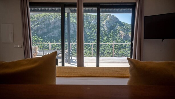 Ein Zimmer mit einem Bett, einem Fernseher und Blick auf einen Balkon mit Gartenmöbeln.