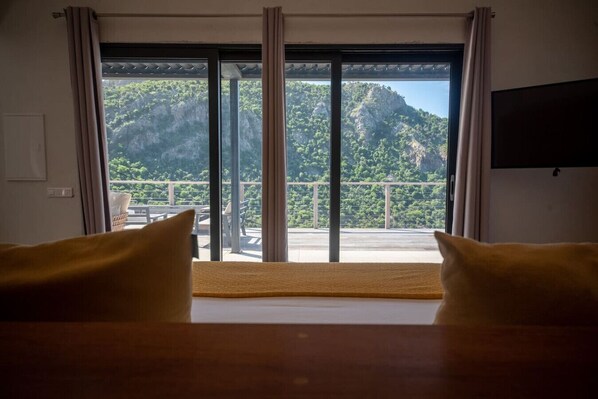 Ein Zimmer mit einem Bett, einem Fernseher und Blick auf einen Balkon mit Gartenmöbeln.