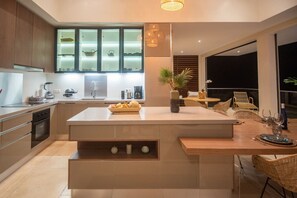A modern kitchen with a central island, built-in appliances, and a dining area with wicker furniture. - Sweet Hill - Villa Rosa (Petite Saline)