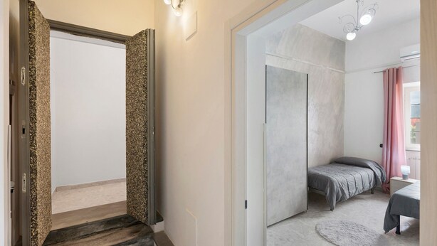 Un dormitorio con cama, mesita de noche, alfombra redonda y ventana con cortinas.
