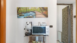 Una cocina con microondas, cafetera y una pequeña mesa con tazas.