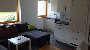Ett modernt vardagsrum med en soffa, ett litet bord och en köksdel med skåp och ett fönster.