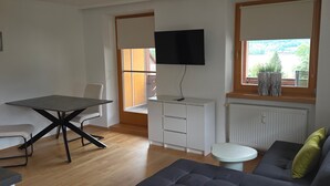 Ett modernt vardagsrum med en soffa, ett matbord, en tv och ett fönster med utsikt.