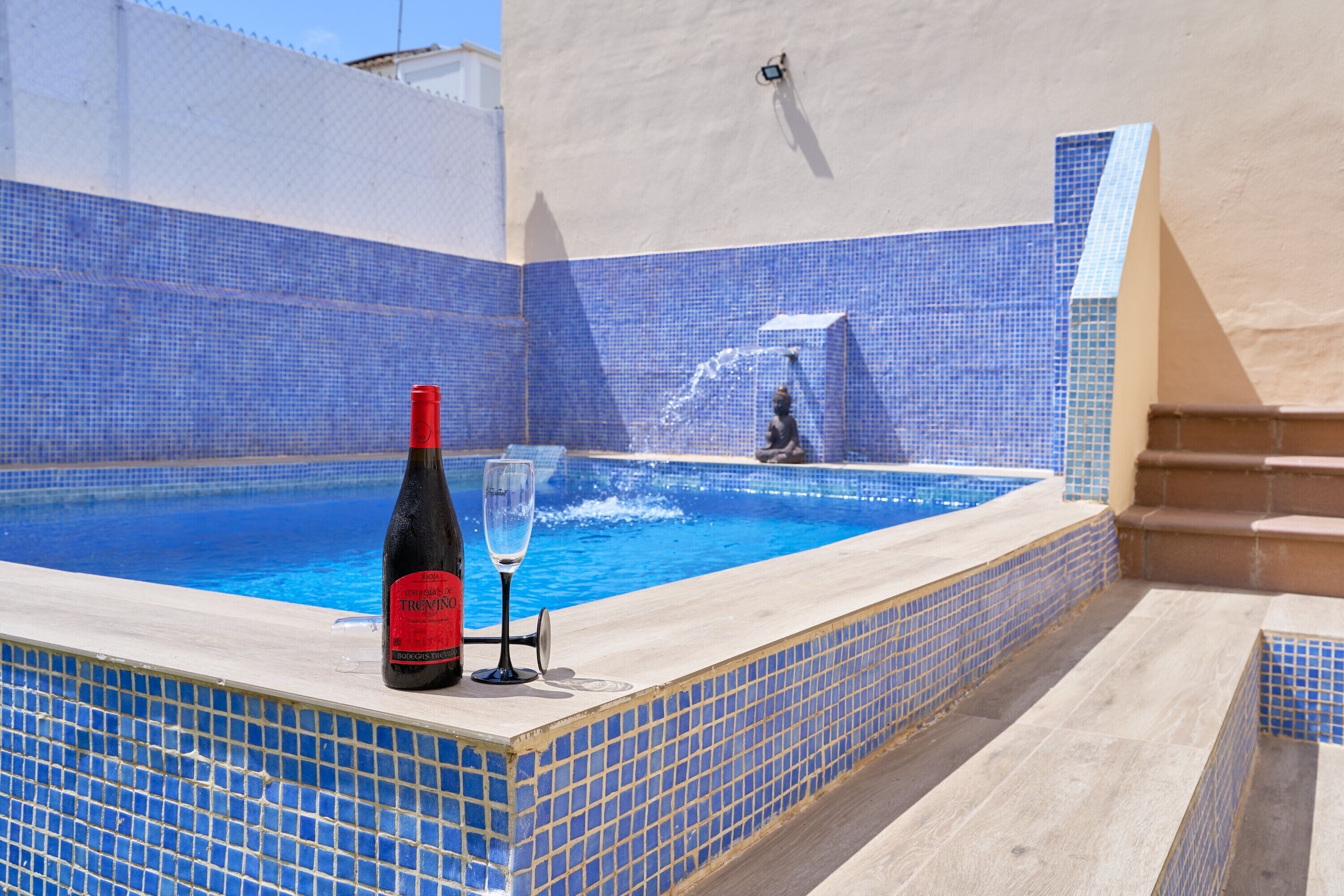 Een zwembad met blauwe mozaïektegels, een fles wijn en een glas op de rand.