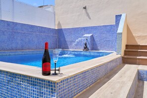 Een zwembad met blauwe mozaïektegels, een fles wijn en een glas op de rand.