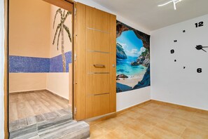 Een kamer met een houten deur, betegelde vloer, een wandklok en een muurschildering van een strand.