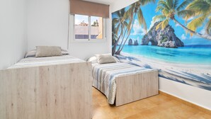 A bedroom with two beds, a window with a view, and a beach-themed mural on the wall. - Villa Oasis del Sol II – Pool – Sea Views (Urbanización Cerro Garbancito)