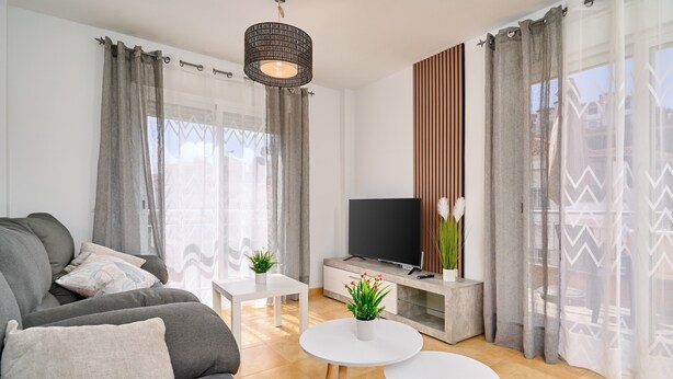 A modern living room with a sofa, TV, white coffee table, and potted plants. - Villa Oasis del Sol II – Pool – Sea Views (Urbanización Cerro Garbancito)