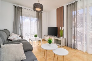 Een moderne woonkamer met een bank, televisie, een witte salontafel en potplanten.