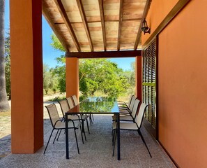 A covered outdoor seating area with a table and chairs, a view of greenery, and a building with orange walls. - Charming rustic home in Alaró, perfect for families and groups amid nature (Alaró)