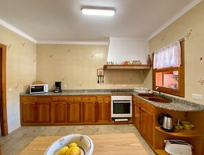 Eine Küche mit Holzschränken, einer Mikrowelle, einem Herd, einer Spüle und einem Fenster mit Spitzenvorhängen.