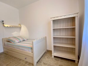 Ein Schlafzimmer mit einem Einzelbett, einem weißen Kleiderschrank und einem kleinen Regal mit einer Lampe.