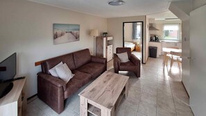 Un salon comprenant un canapé, un fauteuil et une table basse, une télévision et un tableau accroché au mur.