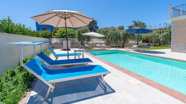 A swimming pool with lounge chairs and umbrellas, surrounded by greenery and a building. - Apartment 'Milu' Poolside, Wi-Fi and Air Conditioning (Arenella)