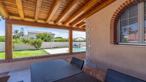 A covered patio with a wooden ceiling, outdoor seating, and a view of a swimming pool and neighboring houses. - Apartment 'Milu' Poolside, Wi-Fi and Air Conditioning (Arenella)