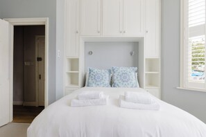 Quarto com uma cama grande, cabeceira branca e duas mesas de cabeceira com abajures.