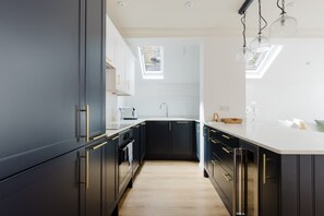 A modern kitchen with dark cabinetry, a white countertop, and a skylight. - Chic 2BDR Flat in Fulham with Patio (London)