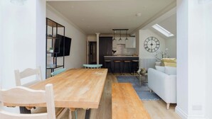 Um interior moderno com uma mesa de jantar de madeira, um sofá, área de cozinha e um relógio de parede grande.