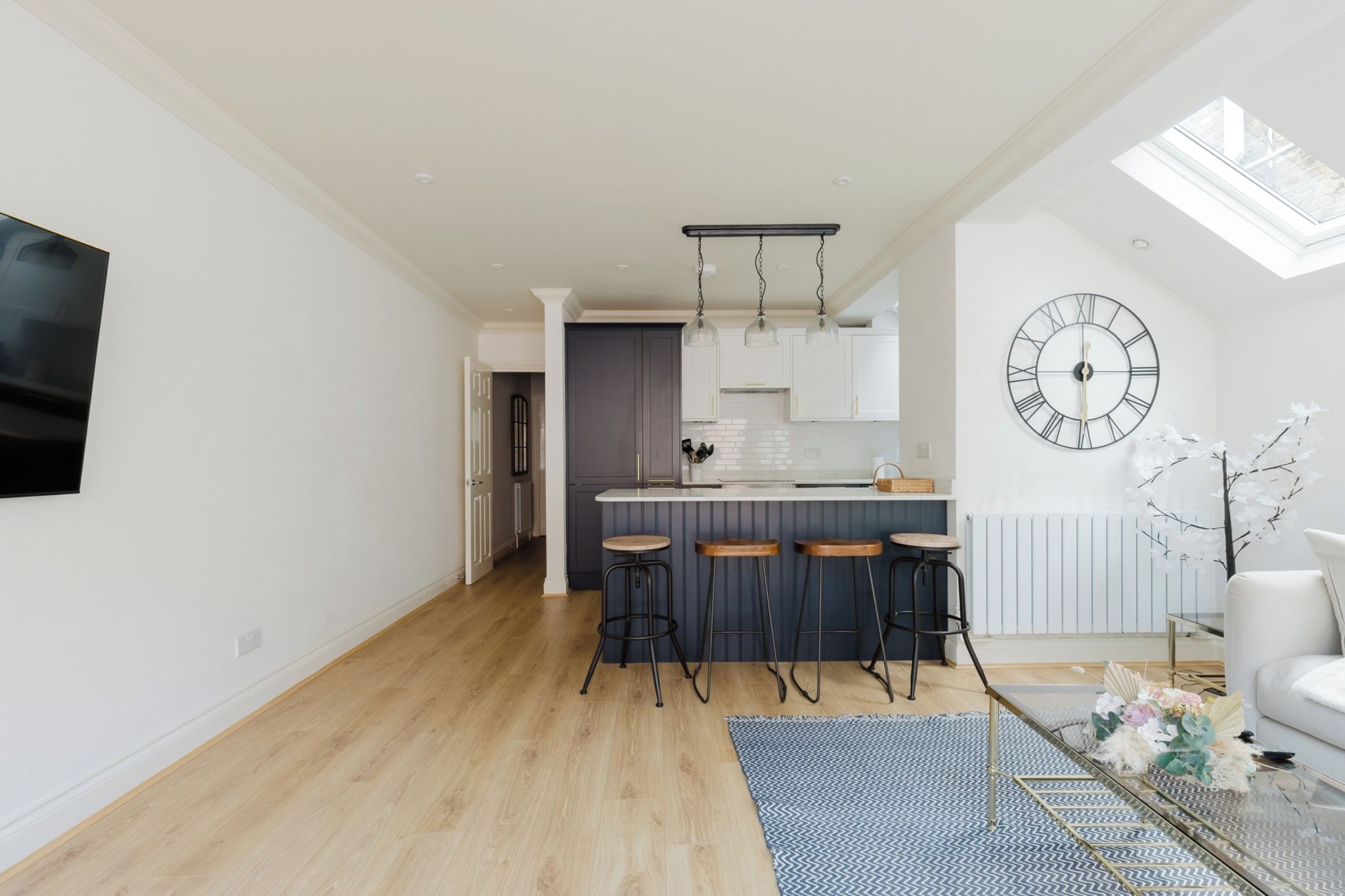 A modern kitchen with a central island, bar stools, and a large wall clock.