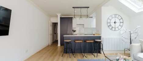 A modern kitchen with a central island, bar stools, and a large wall clock.