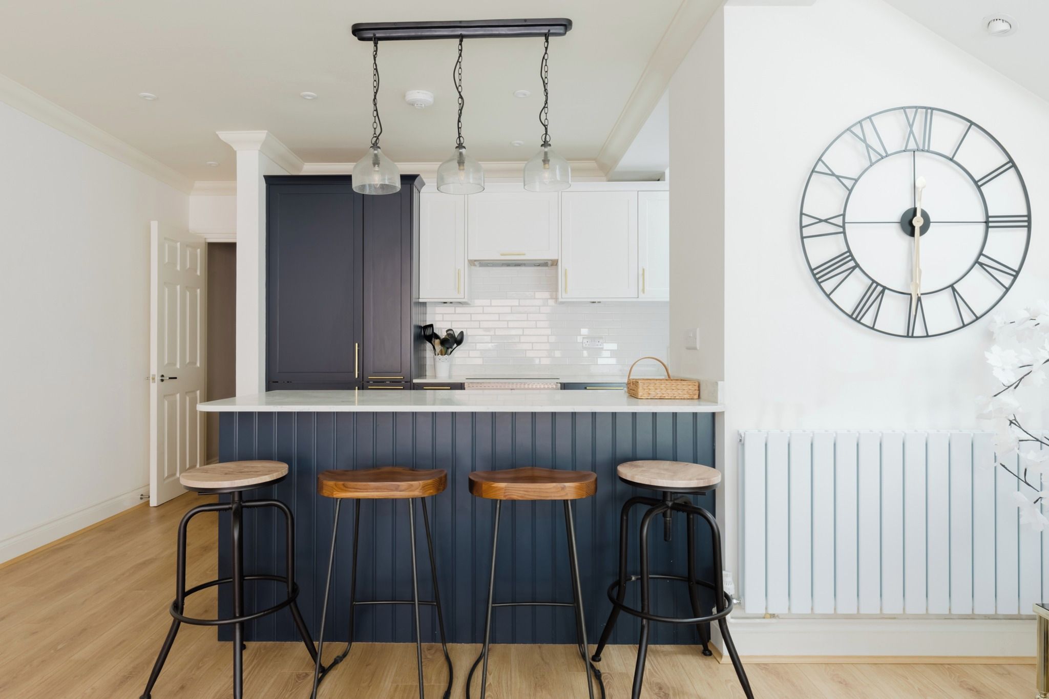 A modern kitchen with a bar area, pendant lights, and a wall clock.