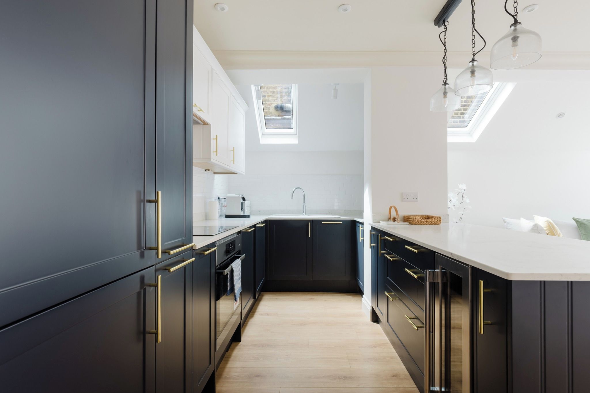 A modern kitchen with dark cabinetry, a white countertop, and a skylight.