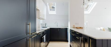 A modern kitchen with dark cabinetry, a white countertop, and a skylight.