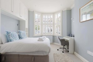 A bedroom with a bed, a desk, and a window with shutters. - Chic 2BDR Flat in Fulham with Patio (London)