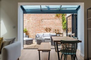 An open-plan living space with a glass ceiling, a brick wall, and a dining area with a table and chairs. - Chic 2BDR Flat in Fulham with Patio (London)