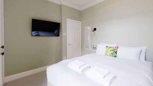 Quarto de hotel com cama, televisão de tela plana na parede, porta e luminária na parede.