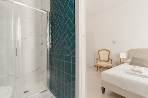 A hotel room with a glass shower enclosure, a bed with white bedding, a wooden chair, and a nightstand with a lamp. - Spacious 100m2 apartment, ideal for up to 6 guests, located on the second floor with lift.Located in the Guastalla district, it is about a 15-minute walk from the M3 Crocetta, M4 Sforza-Policlinico and M1/M4 San Babila metro stops, with numerous surface  (Milan)