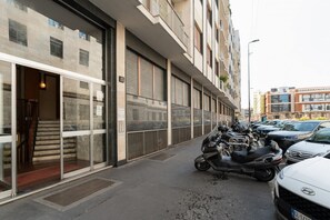 A building with a glass entrance, a parked scooter, and a row of parked cars along the street. - Spacious 100m2 apartment, ideal for up to 6 guests, located on the second floor with lift.Located in the Guastalla district, it is about a 15-minute walk from the M3 Crocetta, M4 Sforza-Policlinico and M1/M4 San Babila metro stops, with numerous surface  (Milan)