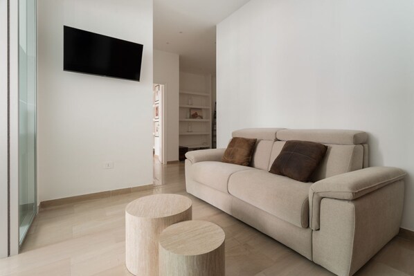 A modern living room with a beige sofa, two wooden side tables, and a flat-screen TV mounted on the wall. - Spacious 100m2 apartment, ideal for up to 6 guests, located on the second floor with lift.Located in the Guastalla district, it is about a 15-minute walk from the M3 Crocetta, M4 Sforza-Policlinico and M1/M4 San Babila metro stops, with numerous surface  (Milan)