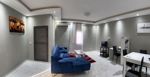 Ein modernes Wohnzimmer mit einem blauen Sofa, einem Esstisch mit Stühlen, einem Fernseher und einem Stadtbild an der Wand.