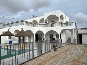 Un bâtiment moderne de couleur blanche, doté de nombreux balcons, d’une piscine et d’un espace extérieur aménagé pour s’asseoir.