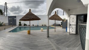 Une piscine agrémentée de deux parasols en chaume, d’une terrasse en bois et offrant une vue sur la mer.