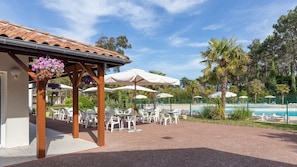 A covered outdoor seating area with tables and chairs, a pool, and palm trees. - House for 4 people with a pool and tennis court (Ondres)
