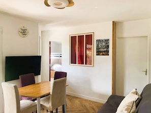 A room with a wooden dining table, two chairs, a sofa, a TV, a door, and a framed picture on the wall. - House for 4 people with a pool and tennis court (Ondres)