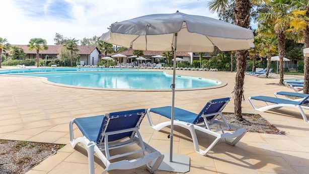 Zona junto a la piscina con sillones, sombrillas, una piscina y palmeras.