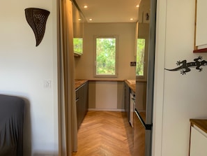 A narrow hallway with a wooden floor, a window with a view of greenery, a kitchen area with cabinets and a refrigerator, and a wall-mounted decorative piece. - House for 4 people with a pool and tennis court (Ondres)