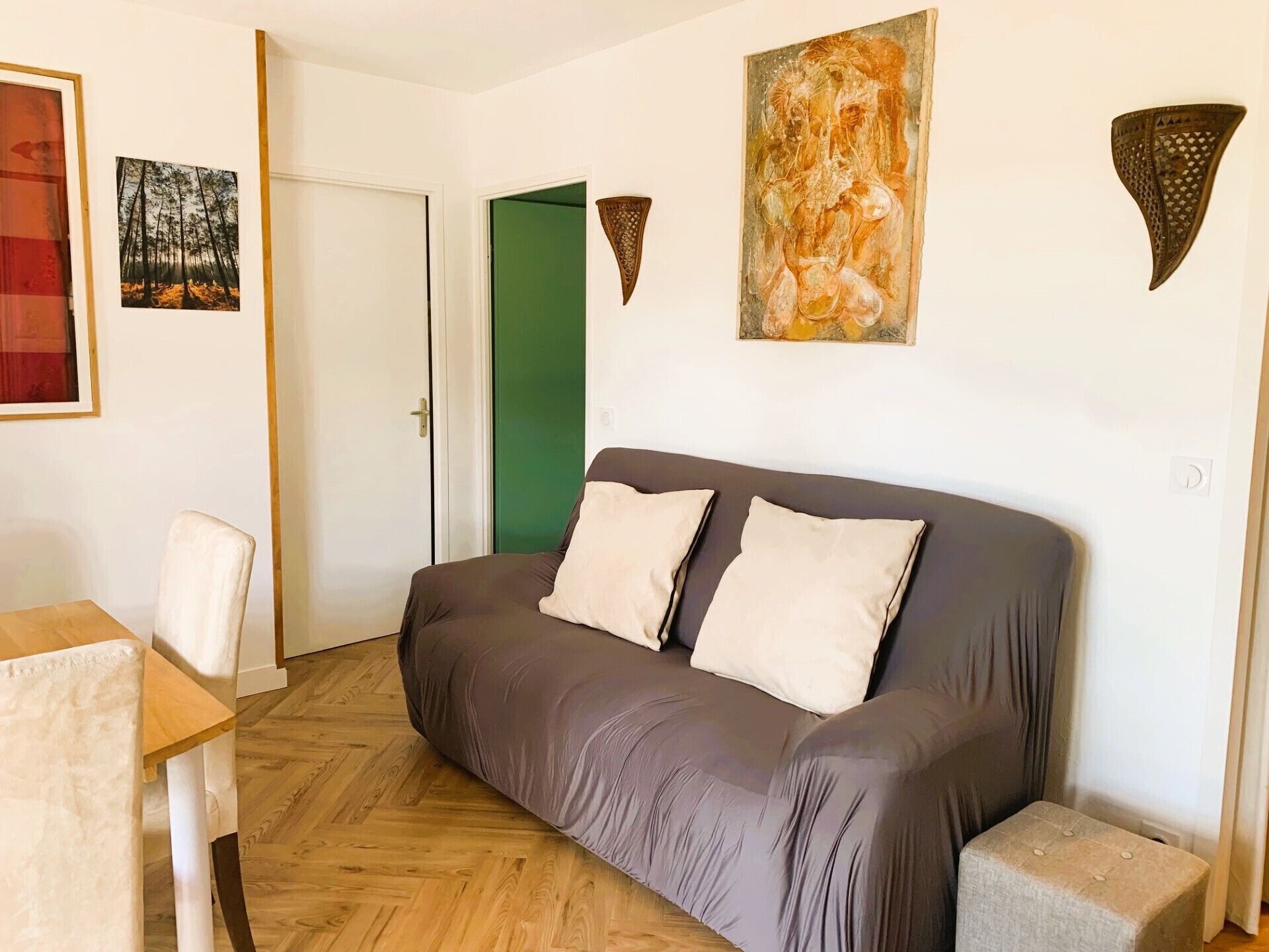 Een kamer met een grijze bank, een houten tafel en twee schilderijen aan de muur.